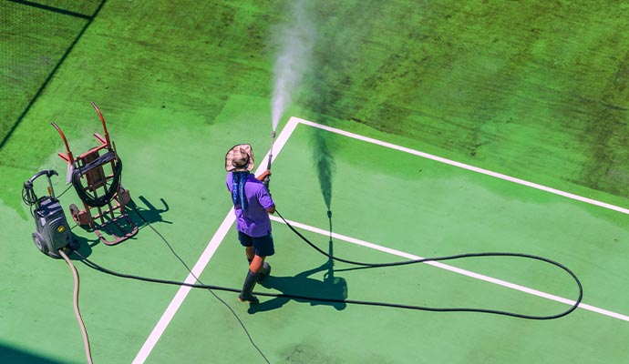 Worker pressure washing green tennis court surface