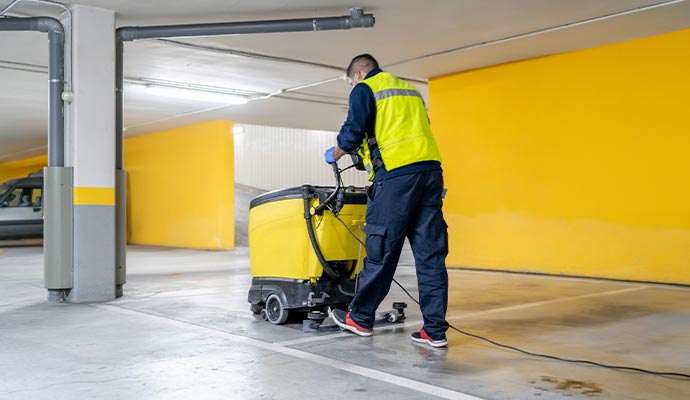 Professional cleaner operating floor scrubber in parking garage