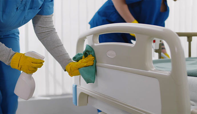 Professional cleaner sanitizing a hospital bed with spray.