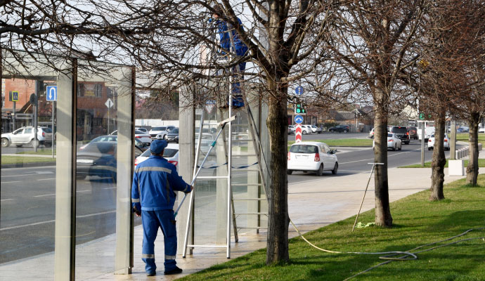 Two professionals cleaning a glass bus station shelter