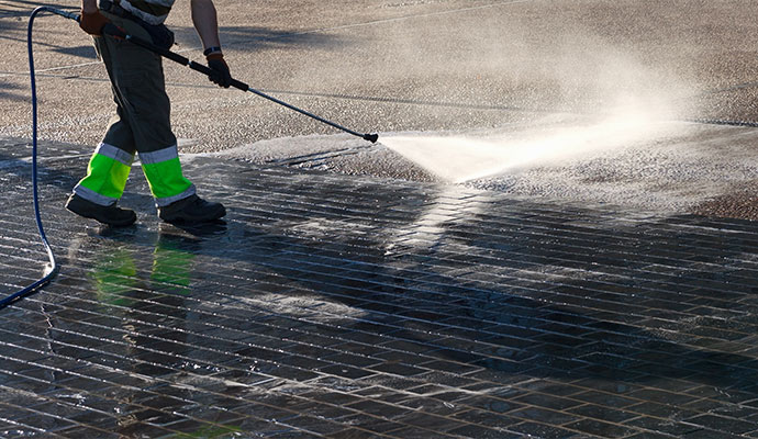 Technician cleaning brick paved driveway with pressure washer