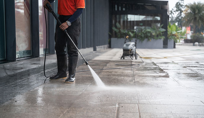 Technician cleaning concrete entryway with pressure washer