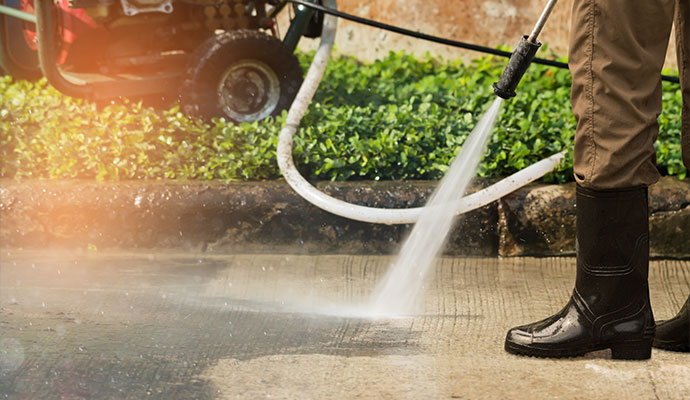 Technician cleaning concrete sidewalk with pressure washer