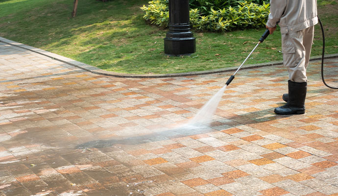 Technician cleaning paved sidewalk with pressure washer