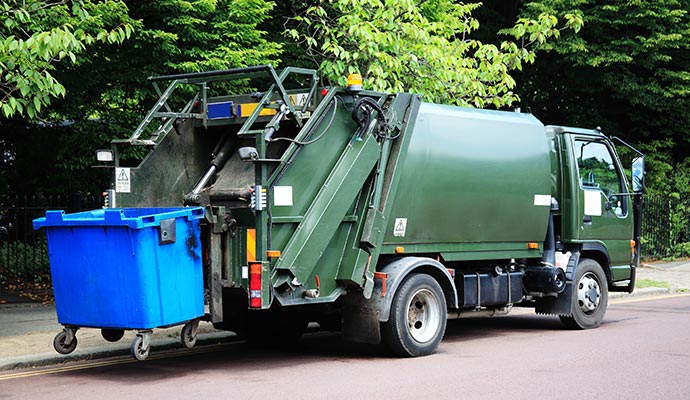Trash pickup service truck collecting a blue dumpster